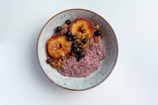 Porridge mit Heidelbeerpulver, gebratenen Pfirsichen, wilden Heidelbeeren und gerösteten Haferflocken