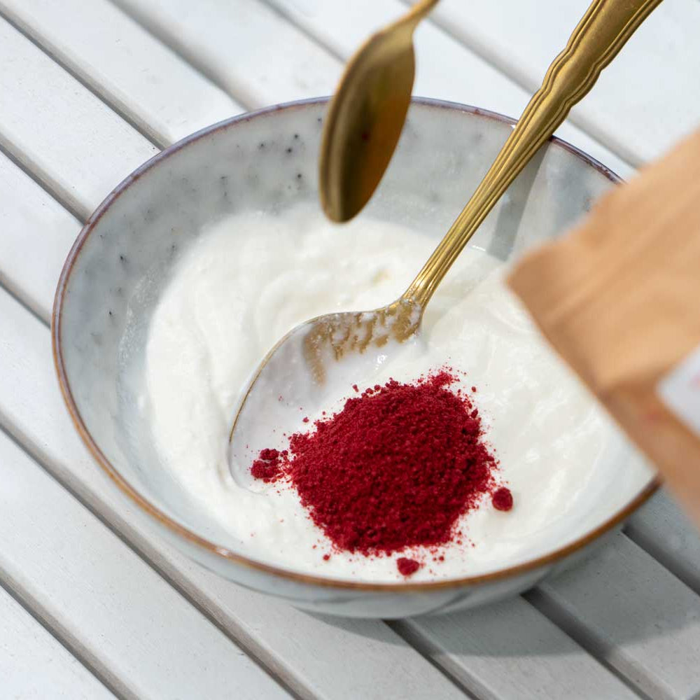 Schale mit rotem Beerenpulver und goldnen Löffeln auf hellem Holztisch