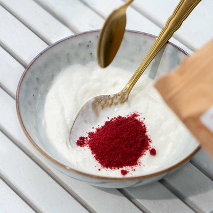 Schale mit rotem Beerenpulver und goldnen Löffeln auf hellem Holztisch