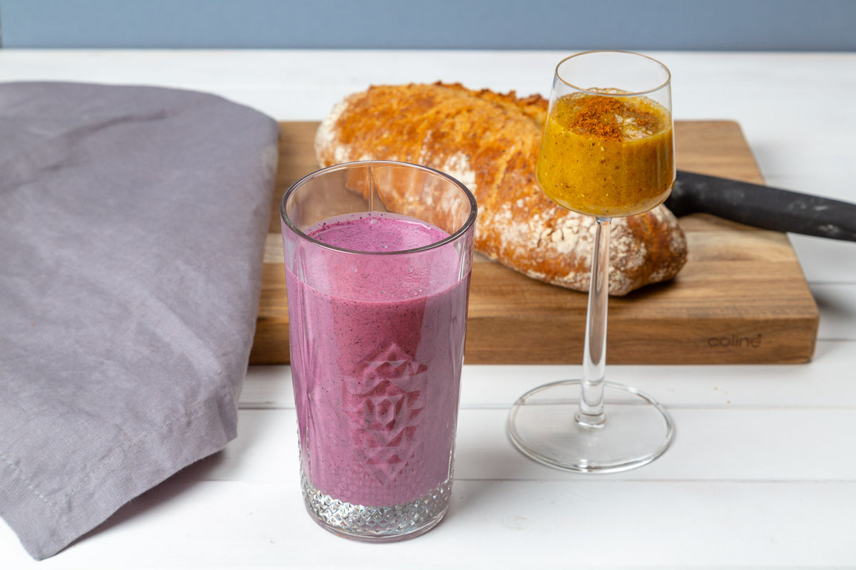 Violetter Heidelbeer-Smoothie im Glas, daneben ein Sanddorn-Shot und frisches Brot