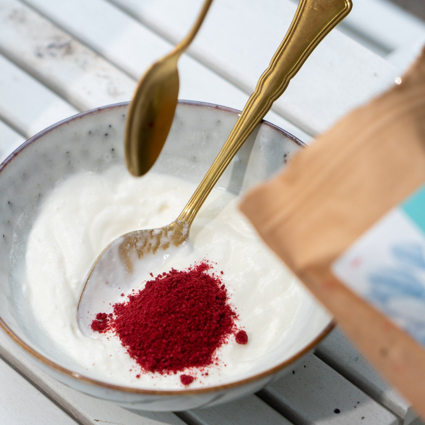 Rotes Preiselbeerpulver wird mit einem goldenen Löffel in eine Schüssel mit weißem Joghurt gegeben.