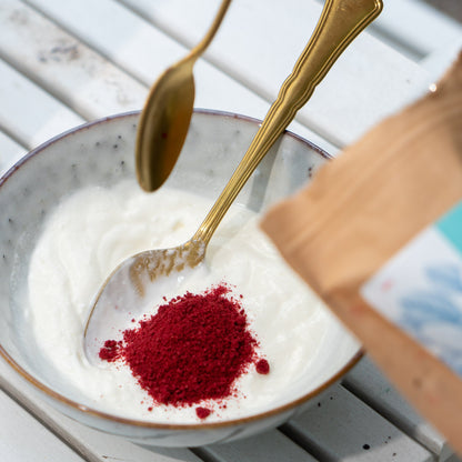 Rotes Preiselbeerpulver wird mit einem goldenen Löffel in eine Schüssel mit weißem Joghurt gegeben.