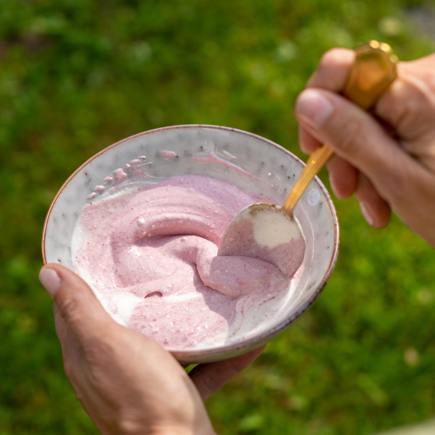 Eine Person hält eine Schüssel mit pinkem Preiselbeerenjoghurt und einem Löffel im Freien.
