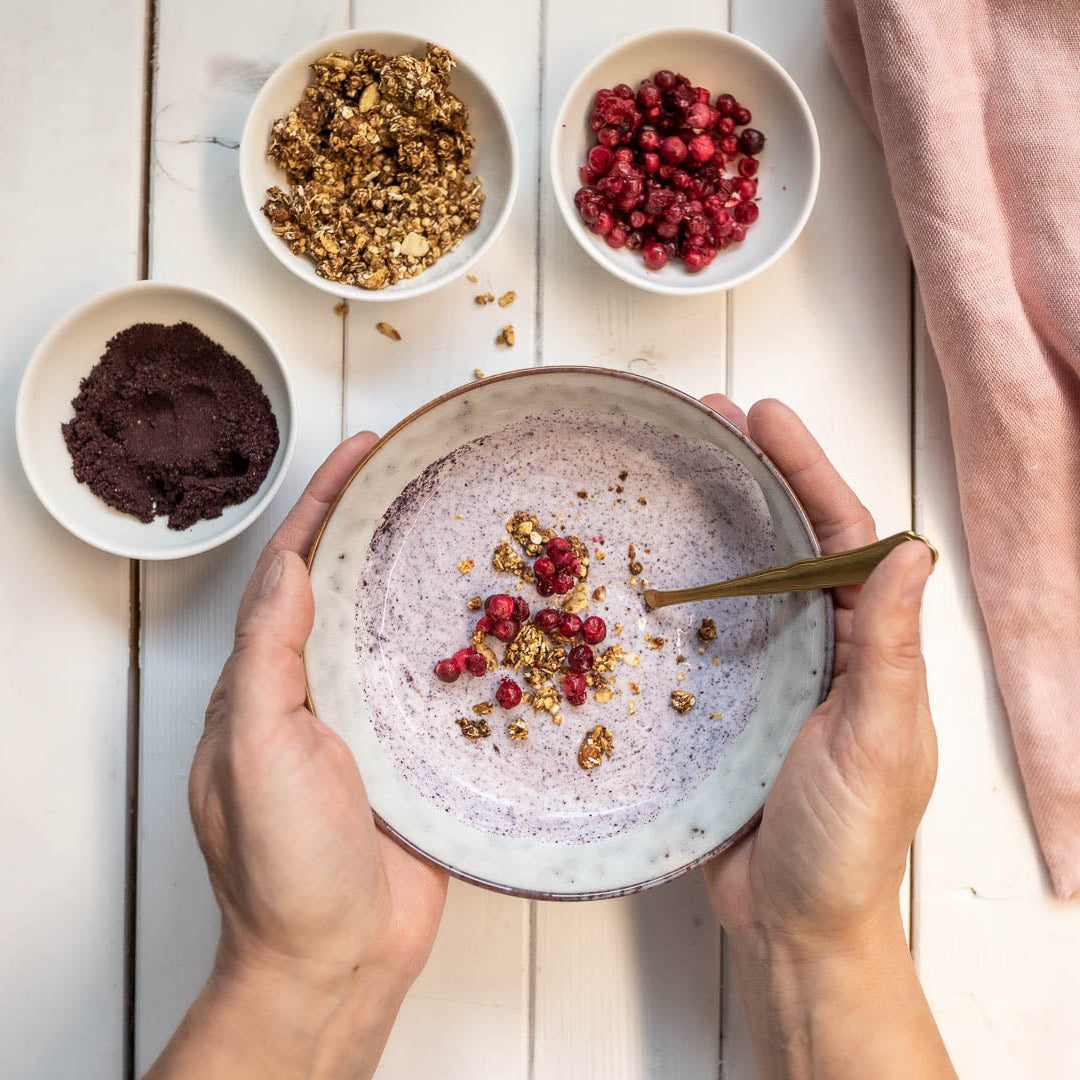 Eine Person hält eine Schüssel Joghurt mit Beerentoppings auf einem Holztisch.