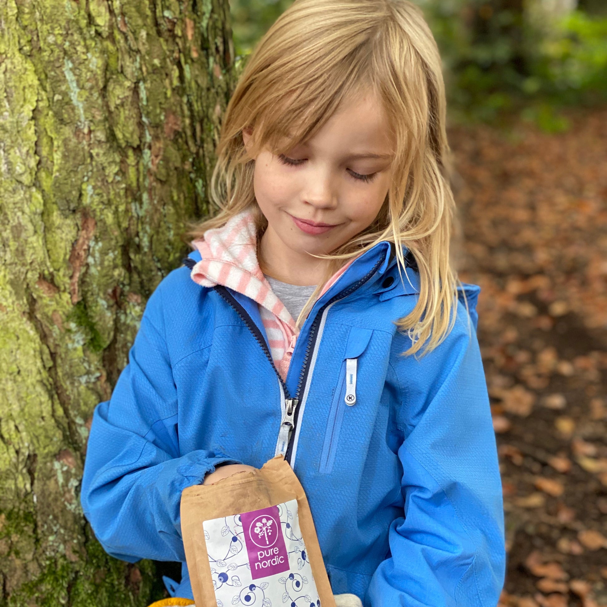 Ein Kind in einer blauen Jacke hält eine Verpackung mit einem Heidelbeerprodukt im Freien.