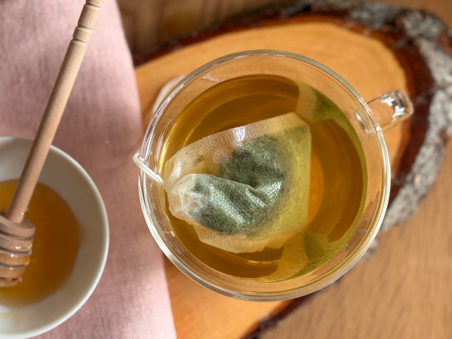 Eine Tasse mit heissem Wasser und einem Teebeutel, gefüllt mit Engelwurzblättern und Honig
