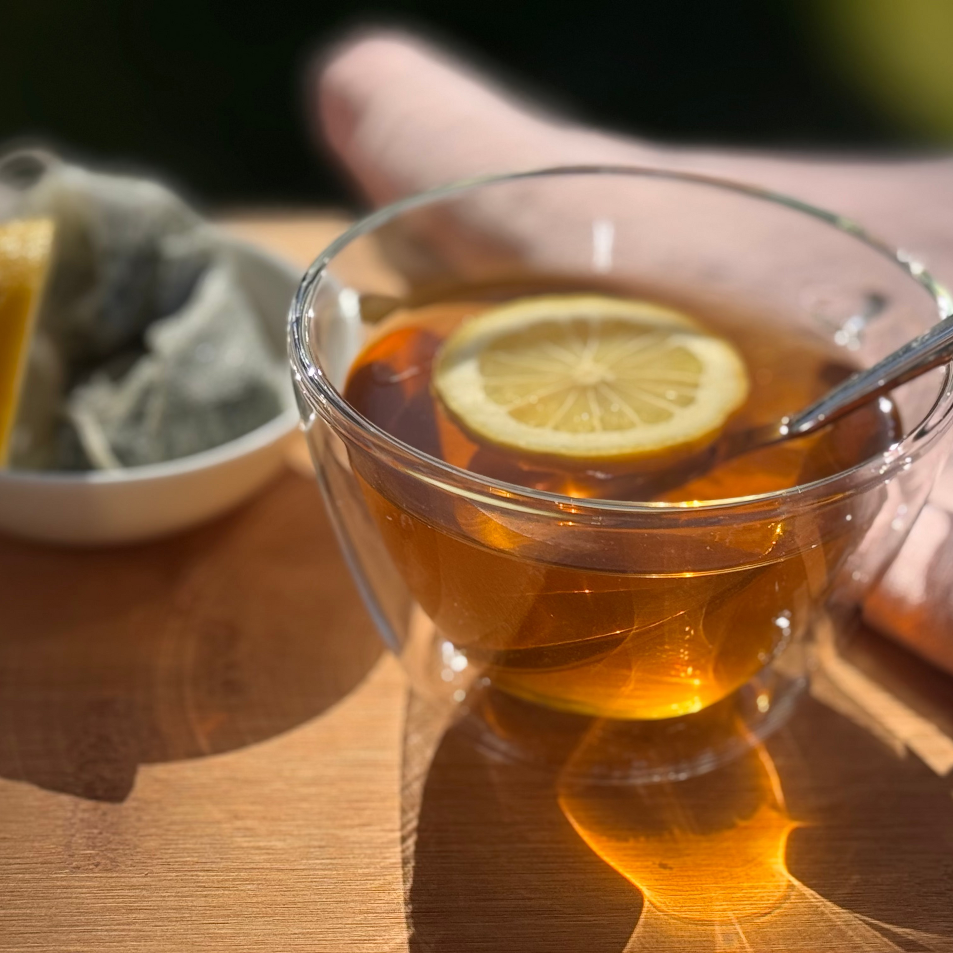 Klares Glas mit heißem Brennnesseltee und einer Zitronenscheibe auf einer Holzoberfläche.