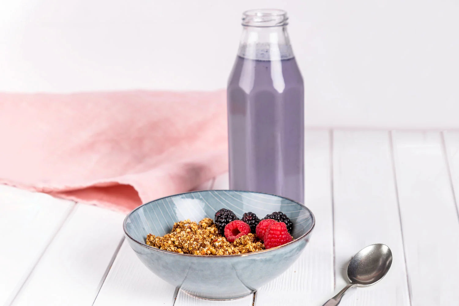 Heidelbeermilch in einer Flasche neben einer Schüssel mit Granola und Beeren