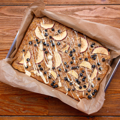 Ein gebackener Kuchen mit Apfelscheiben, gefriergetrockneten Johannisbeeren und drizzled weißer Schokolade auf einem Holztisch.