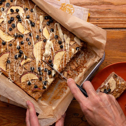Apfelkuchen mit Schwarze Johannisbeeren und Zimt auf einem Holztisch, wobei gerade ein Stück herausgenommen wird.