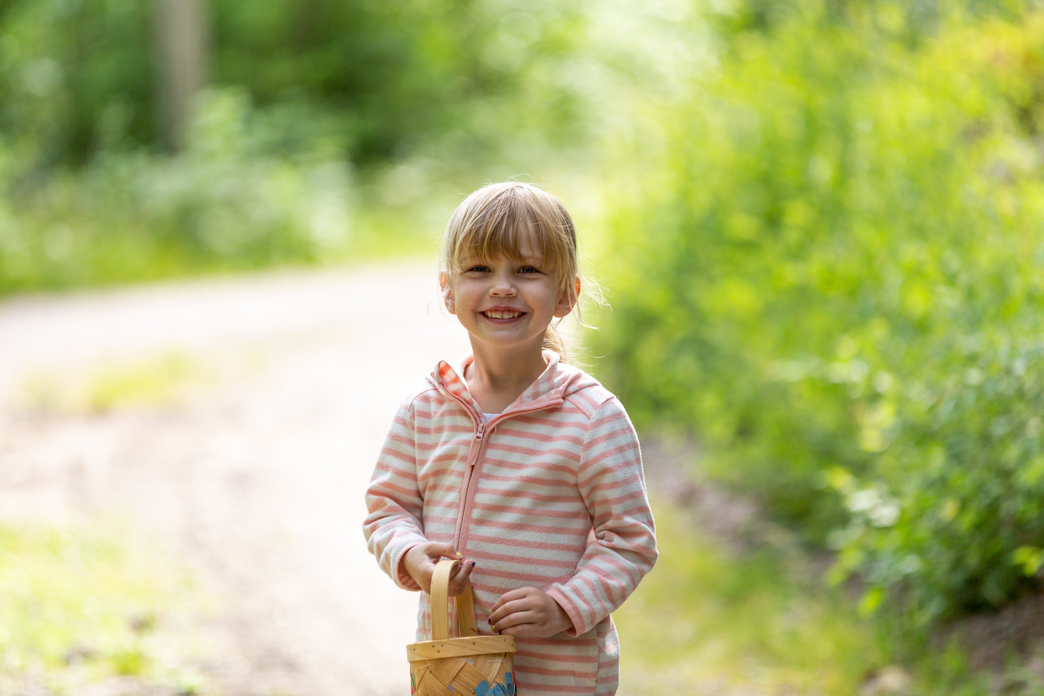 Lächelndes blondes Mädchen mit Korb auf einem Waldweg.