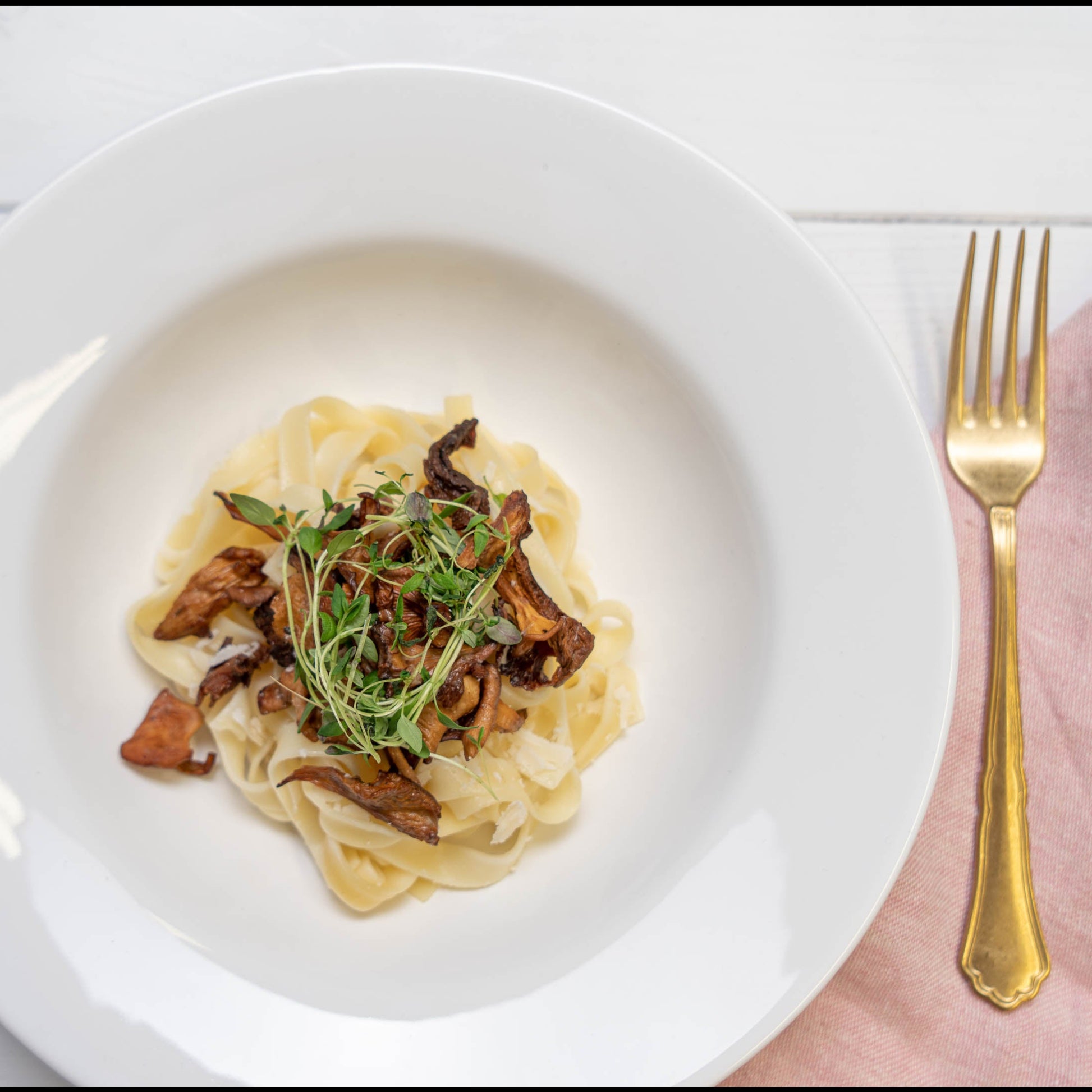 Pastagericht mit gelben Pfifferlingen und Kräutern auf einem weißen Teller, daneben eine goldene Gabel.