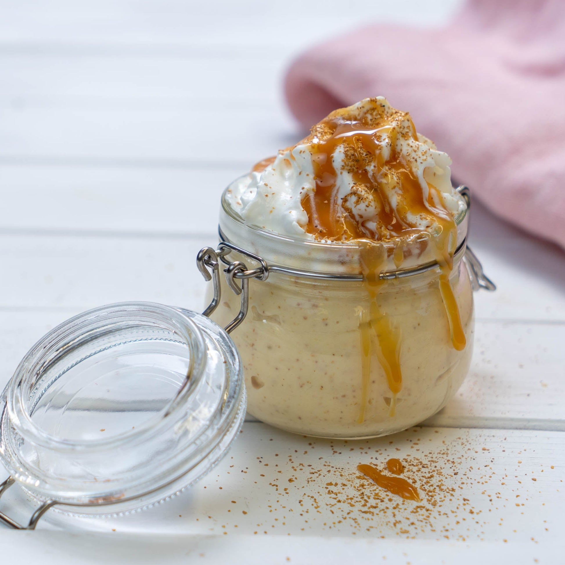 Eine Glasschüssel, gefüllt mit einem Moltebeeren-Dessert, garniert mit Schlagsahne und Karamellsauce auf einem weissen Tisch.