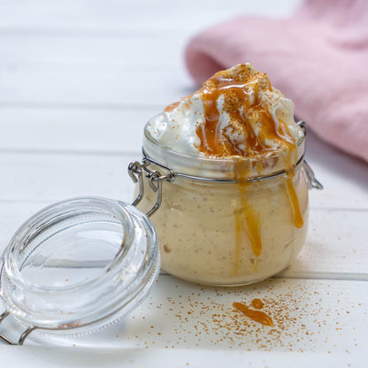 Eine Glasschüssel, gefüllt mit einem Moltebeeren-Dessert, garniert mit Schlagsahne und Karamellsauce auf einem weissen Tisch.