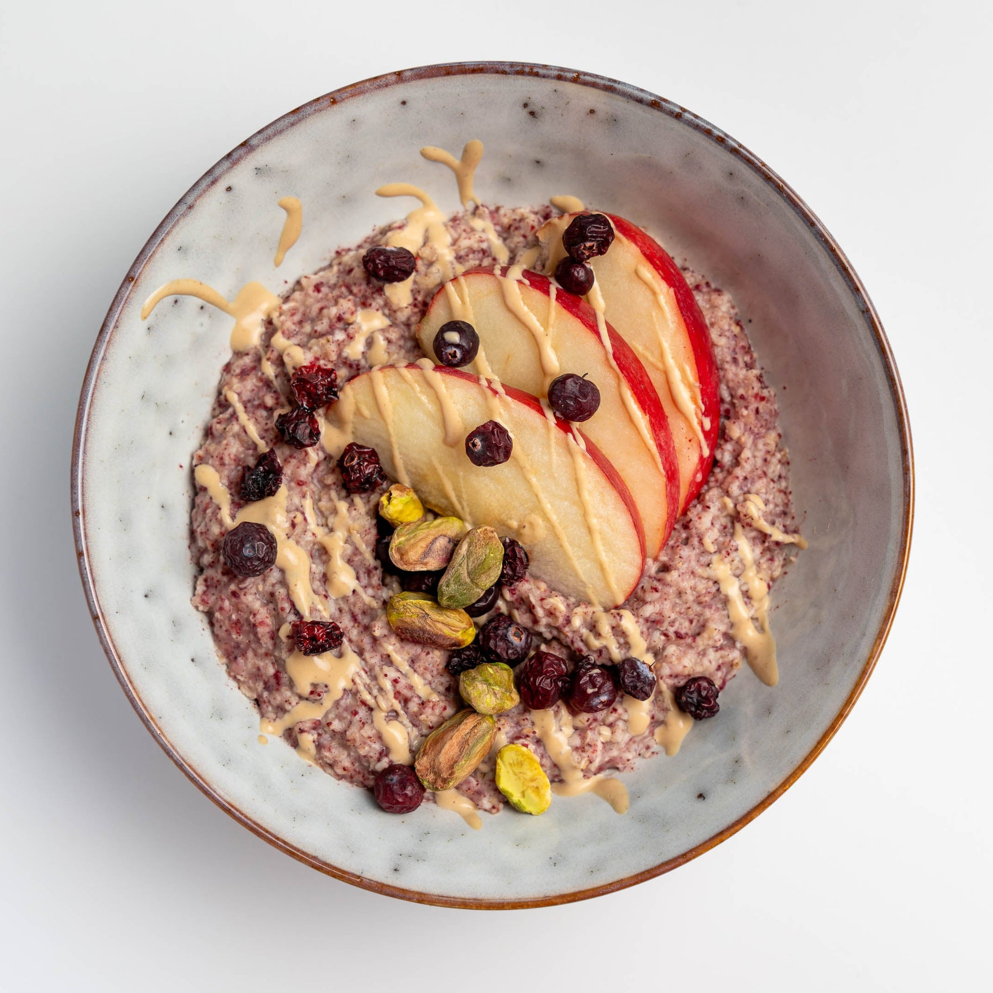 Schale mit Cranberry-Porridge, Apfelscheiben, Nüssen und gefriergetrockneten Cranberries