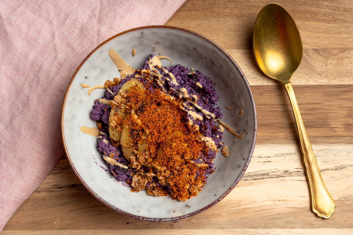 Violettes Porridge mit Heidelbeerpulver, gebratener Banane und Crumble in einer Keramikschale