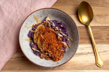 Violettes Porridge mit Heidelbeerpulver, gebratener Banane und Crumble in einer Keramikschale