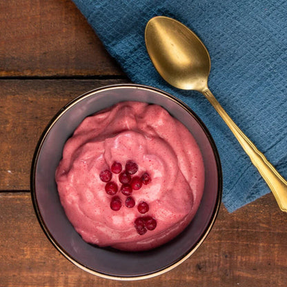 Ein pinkes, schaumiges Preiselbeerdessert in einer blauen Schüssel mit einem goldenen Löffel auf einem Tisch.