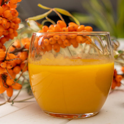 Ein Glas Sanddorn-Orangen-Smoothie mit Sanddornbeeren im Hintergrund.
