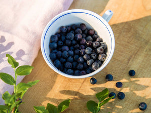 Tasse voller Heidelbeeren auf Holztisch