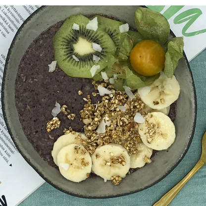 Johannisbeer-Haferbrei in einer Schüssel mit Früchten und Granola auf einem grünen Tischcloth.