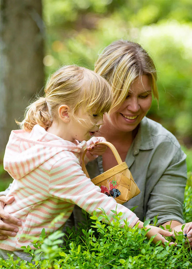 Mutter und Kind pflücken gemeinsam Beeren in Grünen und sammeln sie in einem Korb.