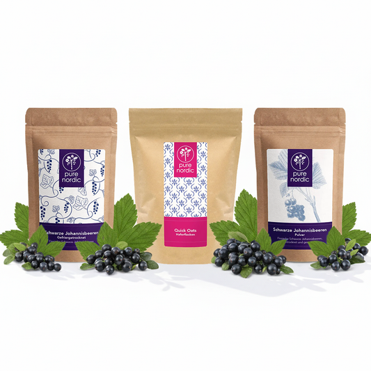 Drei Pure Nordic Beutel mit schwarzen Johannisbeeren und Haferflocken, umgeben von schwarzen Beeren.